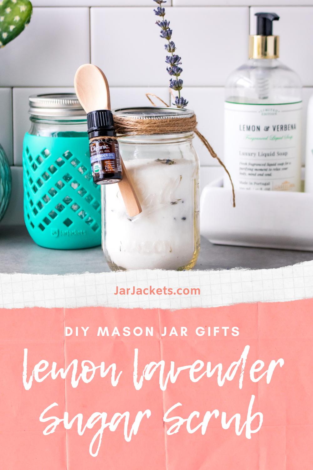 Two Mason jars are full of a body scrub made with lavender buds. One has a small wooden spoon and bottle of lavender essential oil attached to it with twine. 